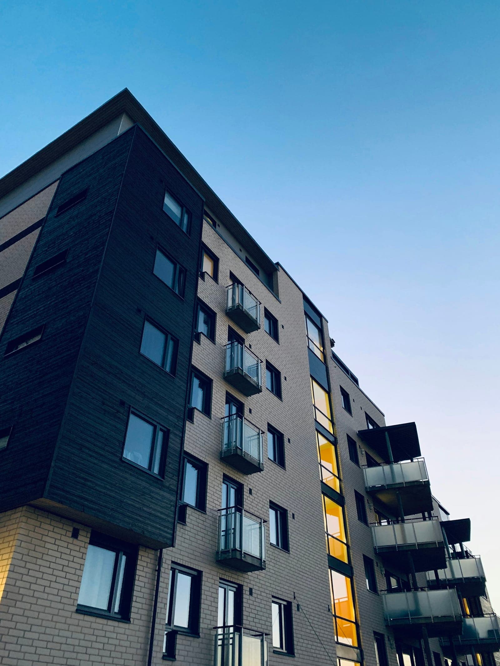Dark-clad apartment tower with glass balconies against a blue sky